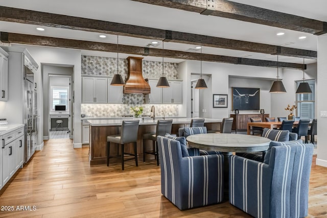 dining room featuring sink, beam ceiling, and light hardwood / wood-style flooring