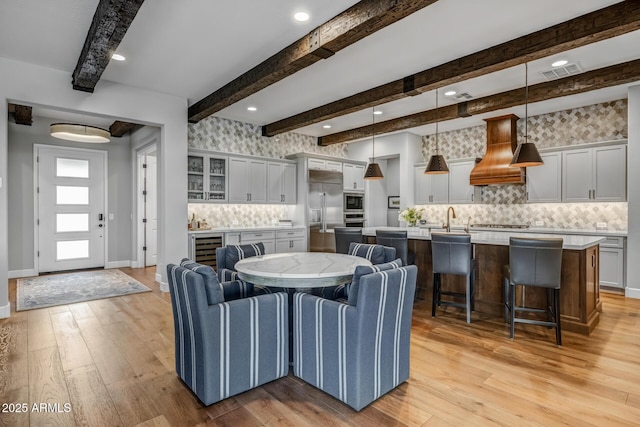 dining room featuring light hardwood / wood-style flooring, wet bar, beverage cooler, and beamed ceiling