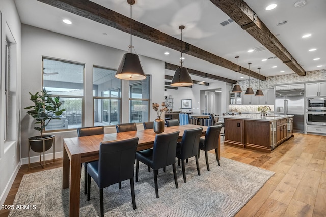 dining space with beam ceiling, sink, and light wood-type flooring