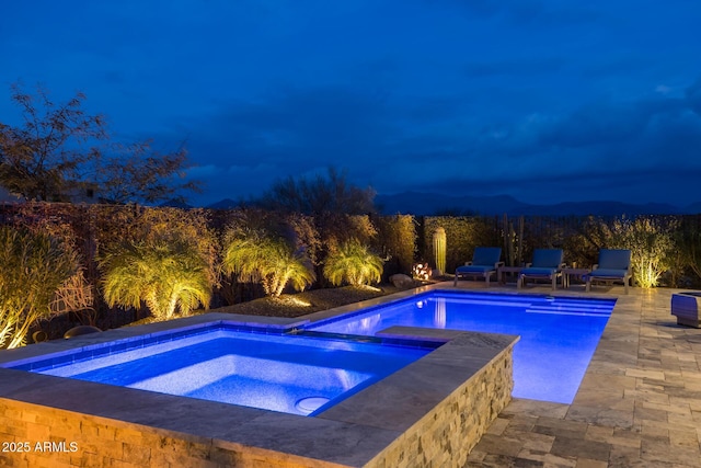 pool at night featuring an in ground hot tub and a patio area