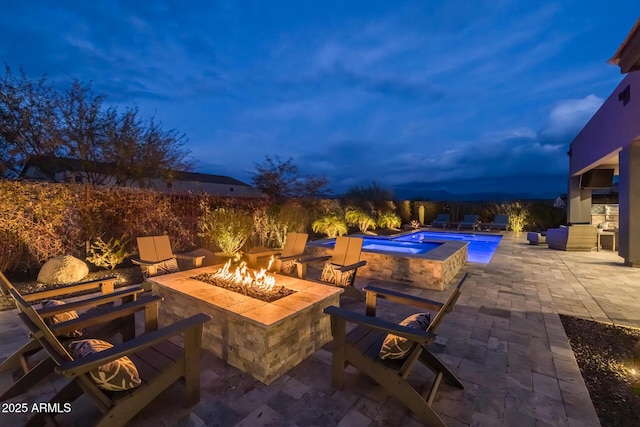 patio terrace at dusk with a swimming pool with hot tub and a fire pit