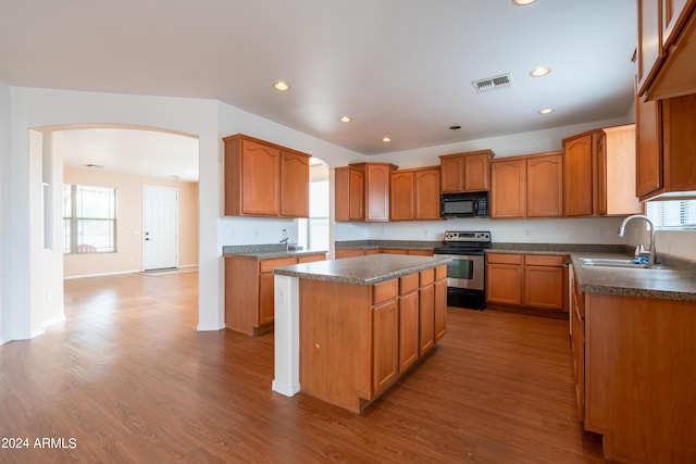 kitchen with electric range, wood finished floors, black microwave, a center island, and arched walkways