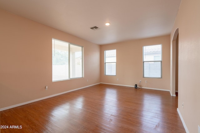 spare room with visible vents, arched walkways, baseboards, and wood finished floors
