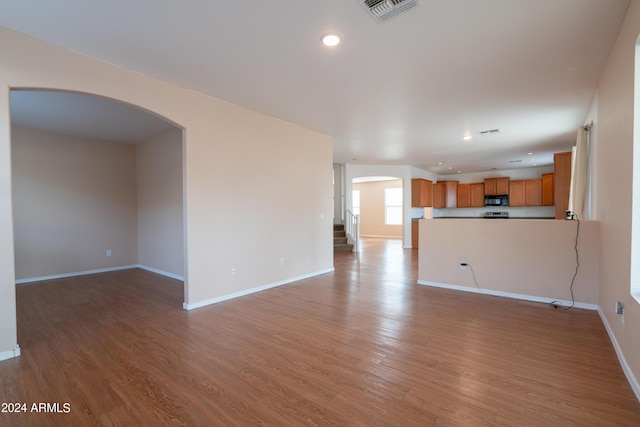 unfurnished living room featuring visible vents, arched walkways, light wood finished floors, and baseboards