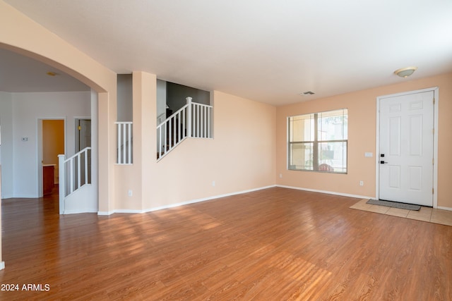 unfurnished living room with light wood-style floors, arched walkways, stairs, baseboards, and visible vents