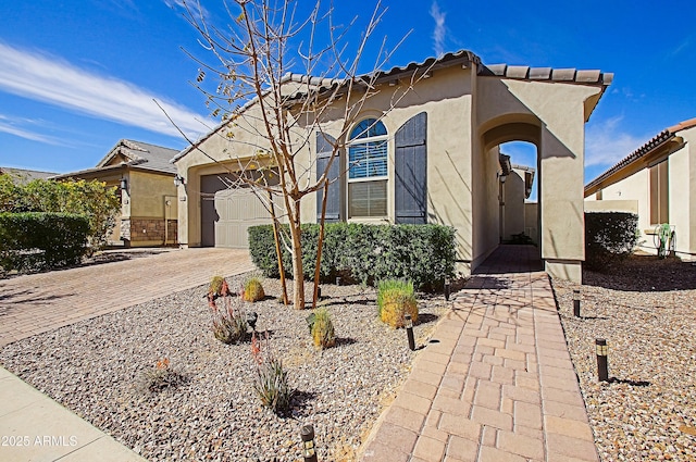 view of front of home featuring decorative driveway, an attached garage, a tile roof, and stucco siding