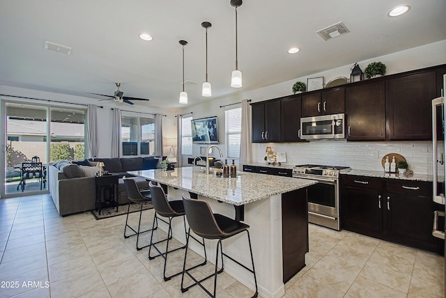 kitchen featuring stainless steel appliances, visible vents, backsplash, a sink, and a kitchen bar