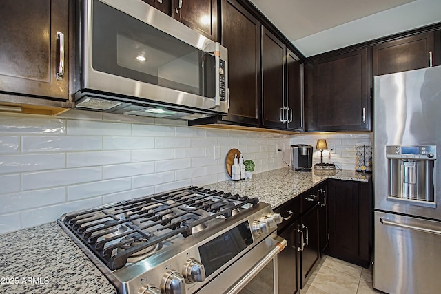 kitchen with stainless steel appliances, dark brown cabinetry, backsplash, and light stone counters