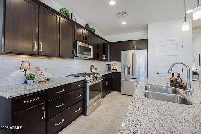 kitchen with appliances with stainless steel finishes, light stone counters, decorative light fixtures, a sink, and backsplash