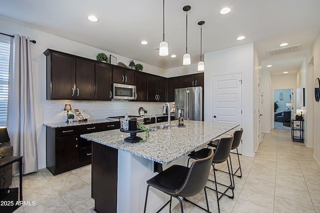 kitchen featuring a sink, visible vents, appliances with stainless steel finishes, backsplash, and light stone countertops