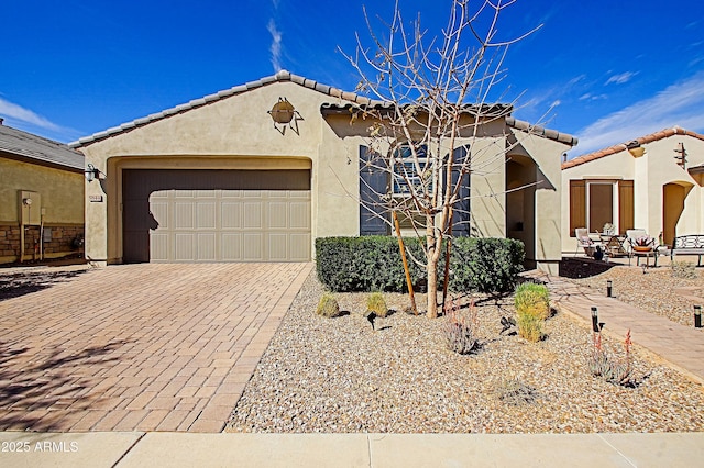 mediterranean / spanish house with a garage, a tiled roof, decorative driveway, and stucco siding