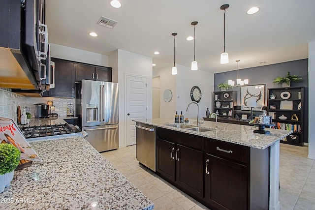 kitchen featuring backsplash, light stone countertops, a kitchen island with sink, stainless steel appliances, and a sink