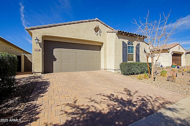 mediterranean / spanish house featuring a garage, decorative driveway, a tile roof, and stucco siding