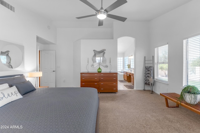 bedroom with ceiling fan, multiple windows, ensuite bathroom, and light colored carpet