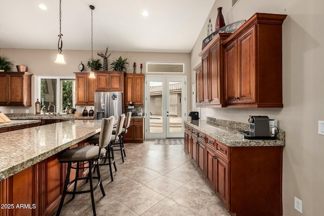 kitchen with light stone counters, stainless steel refrigerator with ice dispenser, french doors, a kitchen bar, and pendant lighting