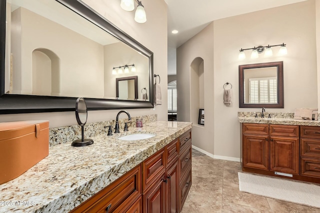 bathroom featuring two vanities, a sink, and baseboards