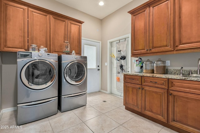 clothes washing area featuring light tile patterned floors, separate washer and dryer, a sink, baseboards, and cabinet space