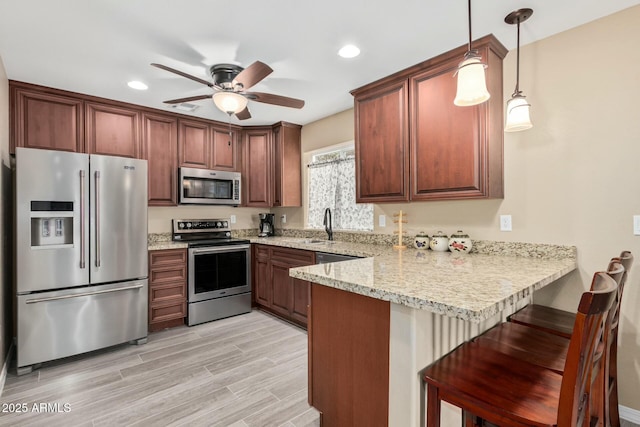 kitchen with decorative light fixtures, a peninsula, stainless steel appliances, light wood-type flooring, and a kitchen bar