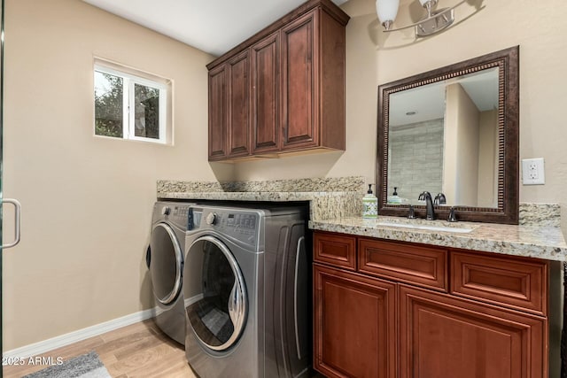 laundry area with light wood finished floors, cabinet space, washing machine and dryer, a sink, and baseboards