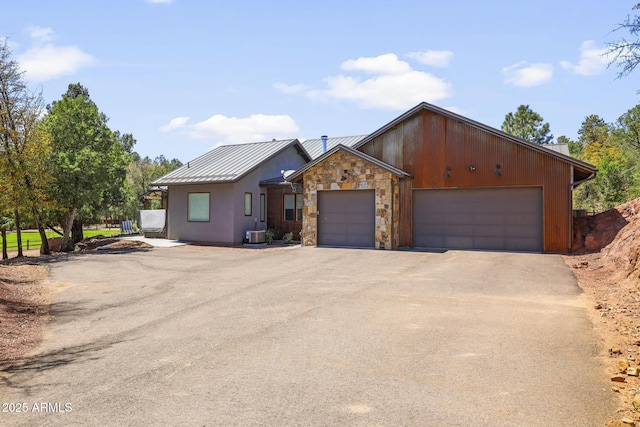 view of front facade with metal roof, fence, stone siding, driveway, and a standing seam roof