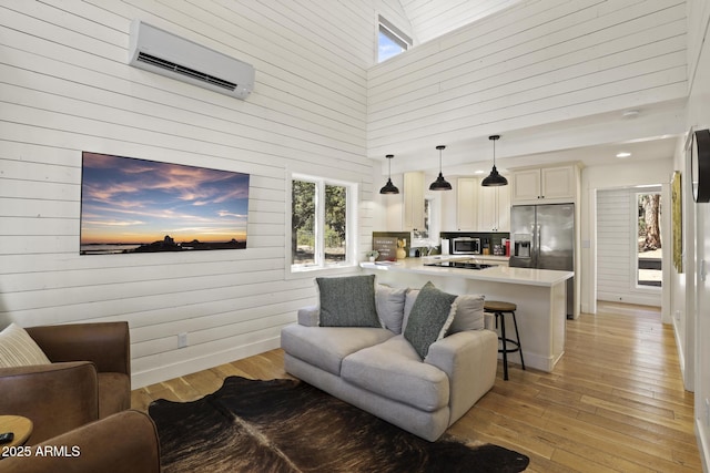 living room with an AC wall unit, a towering ceiling, light wood-style flooring, and baseboards