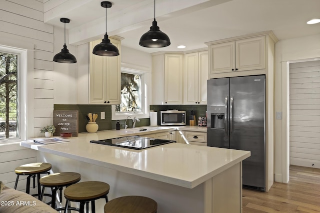 kitchen featuring a breakfast bar, backsplash, appliances with stainless steel finishes, a sink, and a peninsula