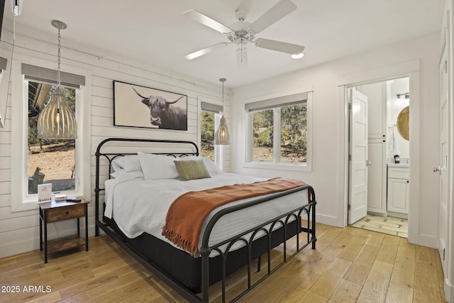 bedroom with light wood finished floors, a ceiling fan, baseboards, and connected bathroom