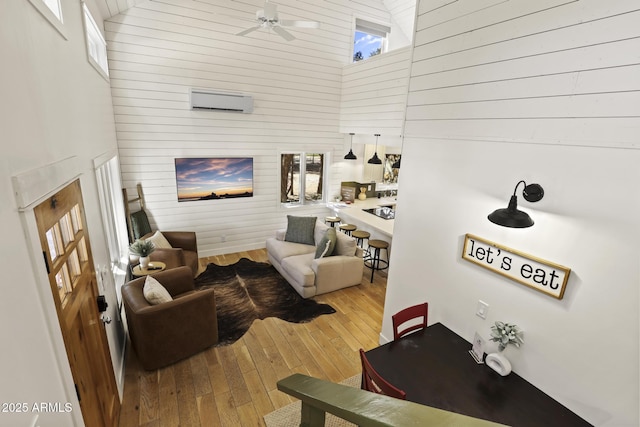 living area with a towering ceiling, wood-type flooring, ceiling fan, and an AC wall unit