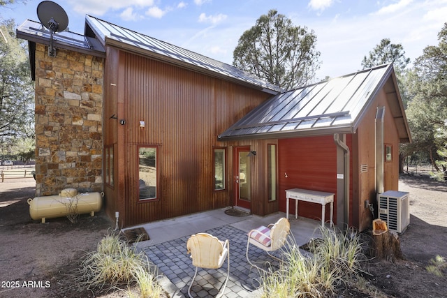 back of property featuring metal roof, a patio, ac unit, stone siding, and a standing seam roof