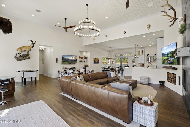 living room with dark wood-style flooring, crown molding, and ceiling fan with notable chandelier