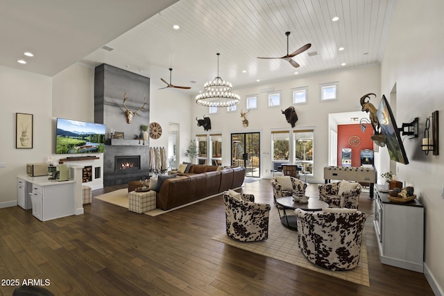 living area with wooden ceiling, ceiling fan, dark wood-type flooring, a lit fireplace, and a high ceiling