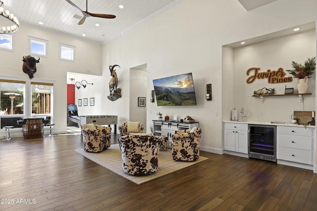 living room featuring a towering ceiling, beverage cooler, crown molding, and dark wood-style flooring