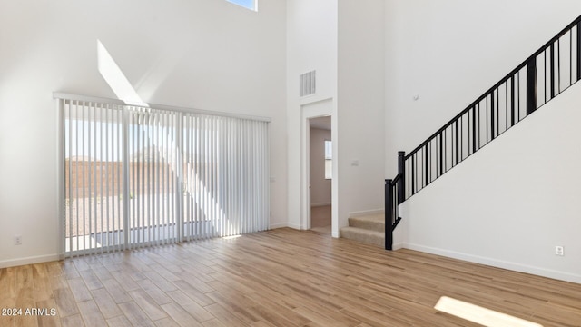 7384 W Buckhorn Trl, Peoria, AZ 85383 - unfurnished living room featuring light wood-style floors, a towering ceiling, baseboards, and stairs