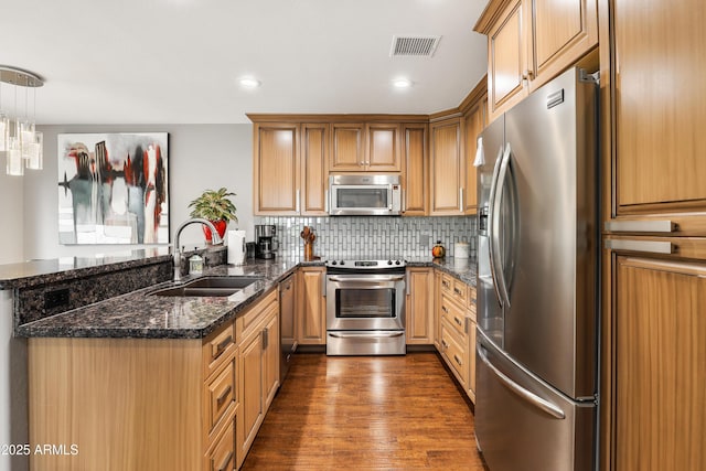 kitchen featuring visible vents, dark wood-type flooring, a peninsula, stainless steel appliances, and a sink