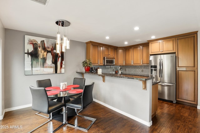 kitchen with appliances with stainless steel finishes, brown cabinets, dark stone countertops, a kitchen breakfast bar, and a peninsula