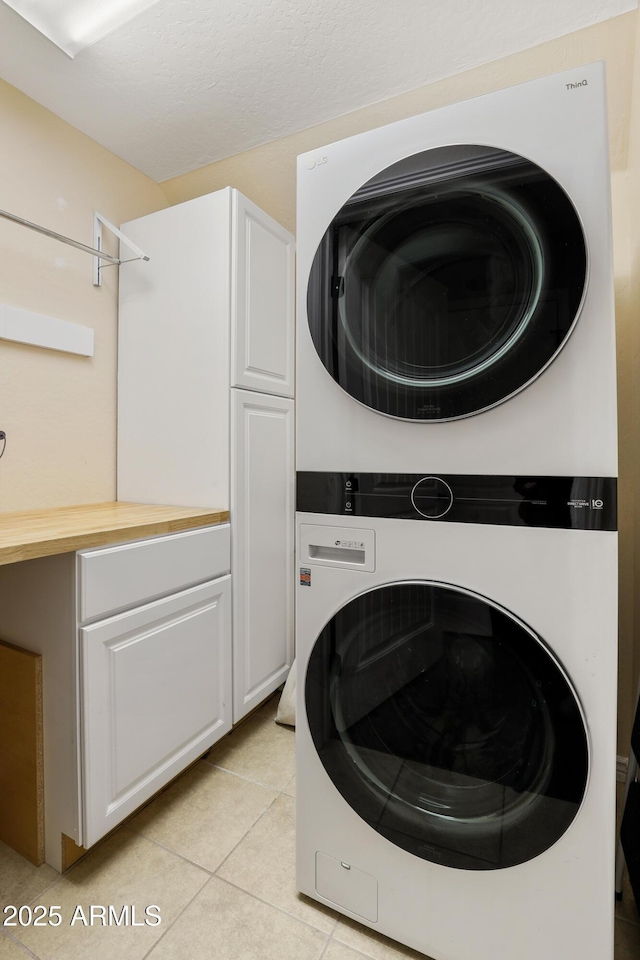 washroom with cabinet space, light tile patterned flooring, and stacked washer and clothes dryer