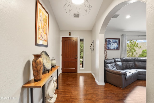 foyer featuring arched walkways, visible vents, dark wood finished floors, and baseboards