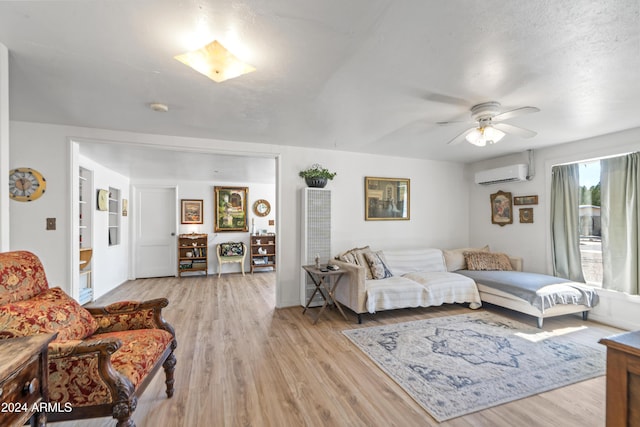 living area with a wall unit AC, light wood-style floors, and a ceiling fan