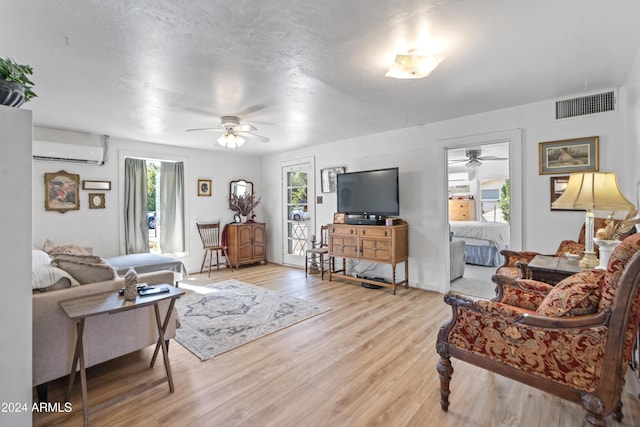 living room featuring light wood-style floors, a ceiling fan, visible vents, and an AC wall unit