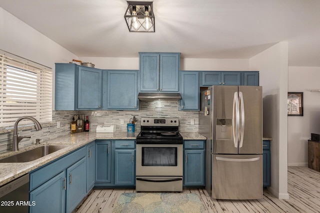 kitchen with light stone countertops, appliances with stainless steel finishes, sink, backsplash, and blue cabinetry