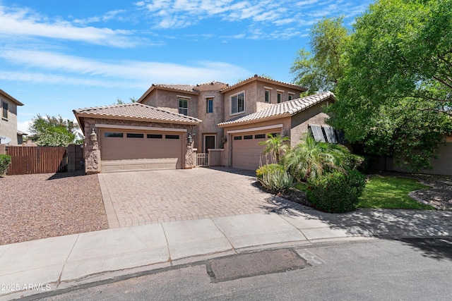 mediterranean / spanish home with fence, decorative driveway, stucco siding, a tiled roof, and an attached garage