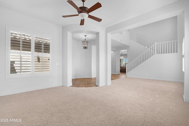 unfurnished living room featuring baseboards, carpet, ceiling fan with notable chandelier, and stairs