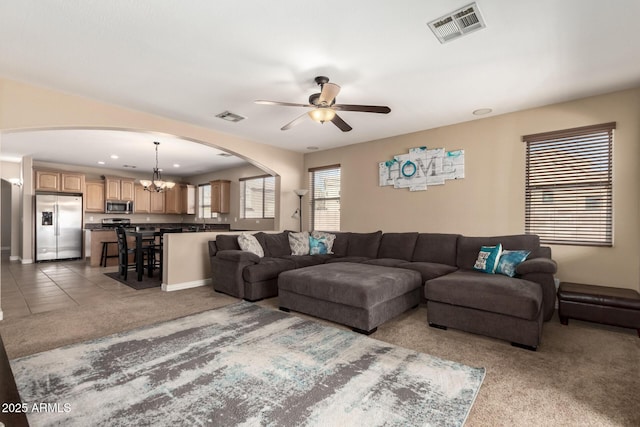 carpeted living area featuring tile patterned flooring, arched walkways, ceiling fan with notable chandelier, and visible vents