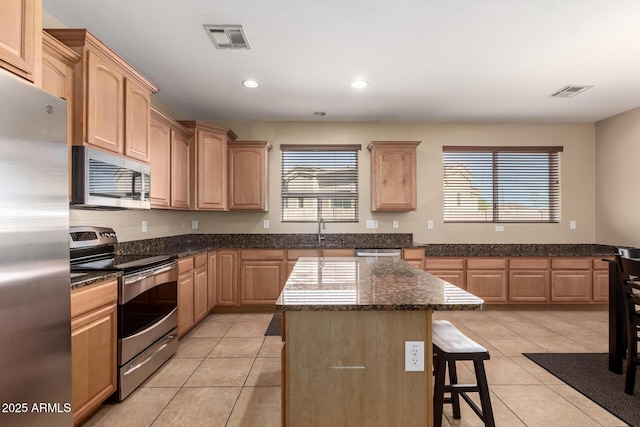 kitchen with light brown cabinets, a kitchen breakfast bar, appliances with stainless steel finishes, light tile patterned floors, and visible vents