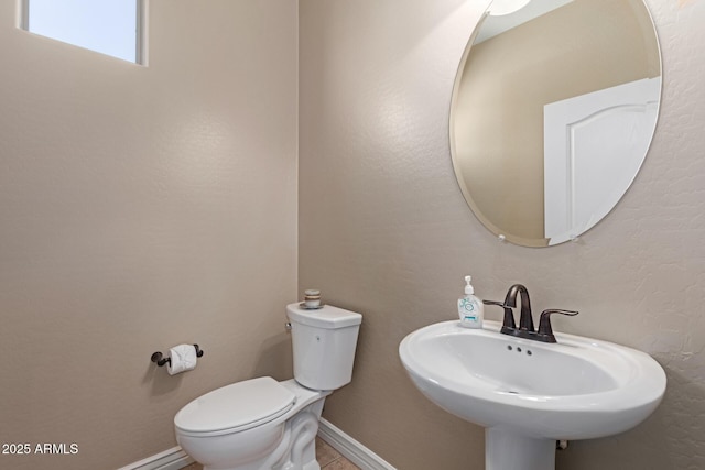 half bath featuring baseboards, a sink, toilet, and tile patterned floors