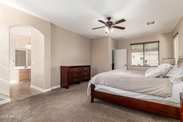 bedroom with baseboards, a sink, arched walkways, visible vents, and light carpet