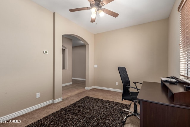 carpeted office space featuring arched walkways, baseboards, and a ceiling fan