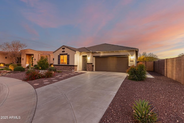 view of front of property featuring stucco siding, fence, stone siding, driveway, and a garage