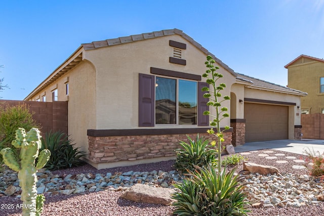 view of front of house with stone siding, concrete driveway, stucco siding, fence, and a garage