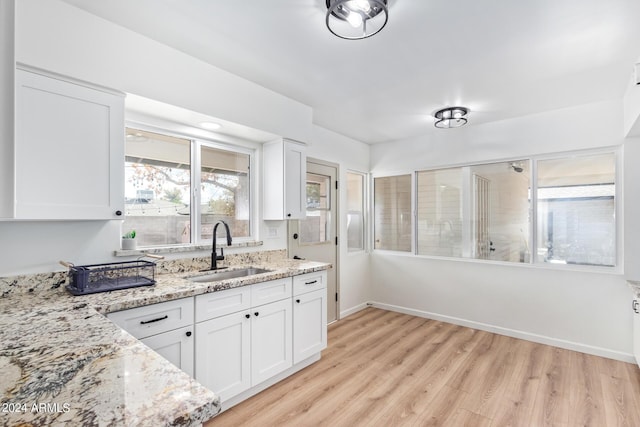 kitchen featuring white cabinetry, baseboards, a sink, light wood finished floors, and light stone countertops